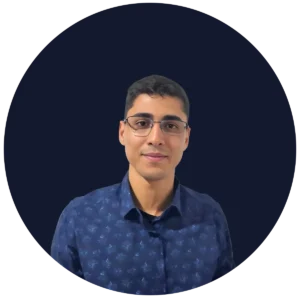 Portrait of a man wearing glasses and a dark blue patterned shirt, smiling at the camera.